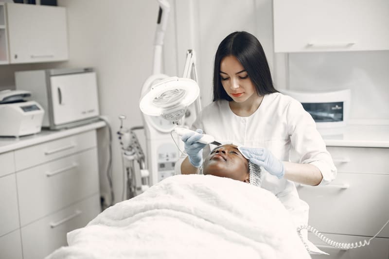 Profesional de una clínica de estética realizando un tratamiento facial a una clienta